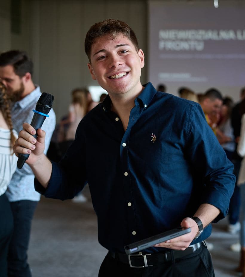 Kacper Wołoszyk z mikrofonem i tabletem podczas prowadzenia wydarzenia networkingowego